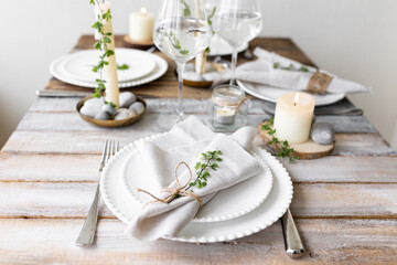 Rustic zero waste wedding decor with natural elements. Wooden table, candles, linen napkins, branches with green leaves. Eco-friendly decoration for the special dinner. Romantic and cozy place