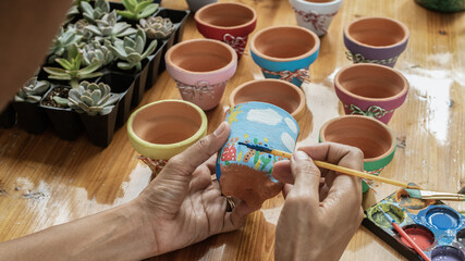 Hands of a Latin woman, painting clay pots to plant succulent plants