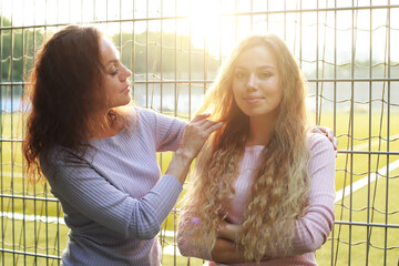 Mother straightens her adult daughter's hair, sunset time, park