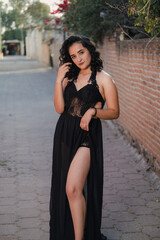 Fototapeta na wymiar Young woman posing in sexy black dress on the street with high heels