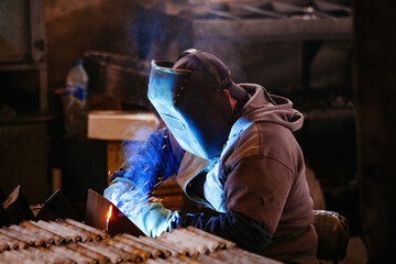 Factory worker in protective mask welding iron parts