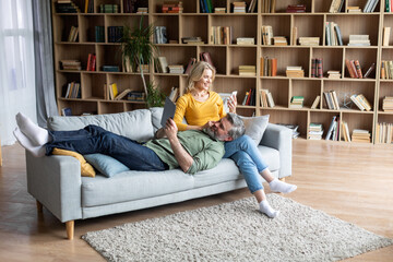 Happy Middle Aged Spouses Relaxing With Modern Gadgets On Couch At Home
