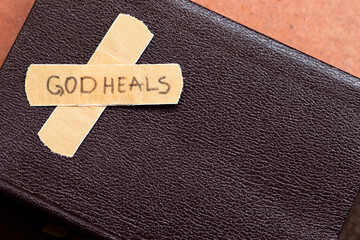 God heals, a handwritten message text on a bandage tape with closed Holy Bible Book with copy...