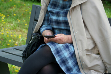 Female with a cell phone. The digital skills of seniors. 50-60 years old businesswoman with a smartphone in her hands sits on a bench, surfing the internet and researching news on social networks.