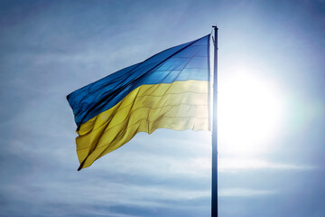 The national flag of the country of Ukraine against the background of the sun and blue sky. Patriotism and national symbol