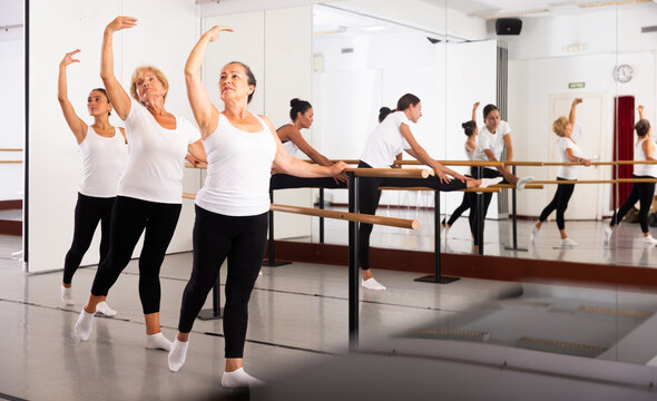 Group of women engaged in classical ballet in a dance studio perform the battement tendu movement, standing in a ballet ..stance near the barre