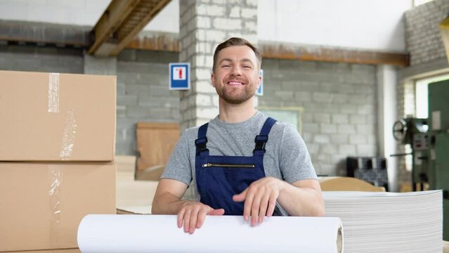 A cheerful worker with a large roll of paper in a printed warehouse depicts a game on drums