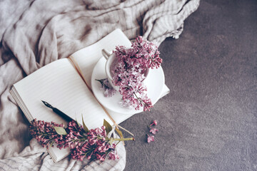 Bouquet of lilacs and an open sketchbook on a table with a women's headscarf in vintage toned...