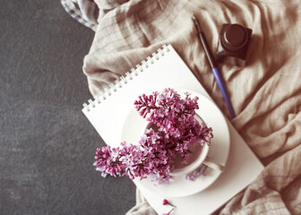 Bouquet of lilacs and an open sketchbook on a table with a women's headscarf in vintage toned colors, top view, soft selective focus. Romantic spring flower background