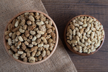 Bowl full of dried mulberry on a wooden background
