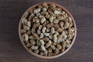 Bowl full of dried mulberry on a wooden background	