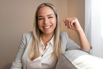 Happy young woman sitting on sofa at home and looking at camera. Portrait of comfortable woman relaxing on armchair. Portrait of beautiful girl smiling and relaxing during autumn.