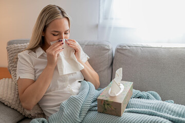 Sick woman sitting under the blanket. Sick woman with seasonal infections, flu, allergy lying in bed. Sick woman covered with a blanket lying in bed with high fever and a flu, resting and drinking tea