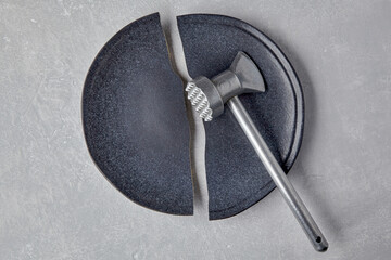 Broken ceramic plate and a kitchen hammer on a light concrete table