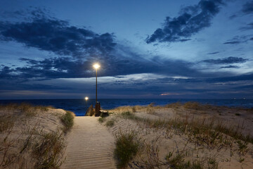 Baltic sea shore at night. Modern wooden pathway (boardwalk). Beach, sand dunes, dune grass. Clear...