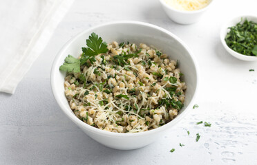 Pearl barley with cheese and herbs in white ceramic bowl on a light gray background, top view. Delicious and healthy breakfast