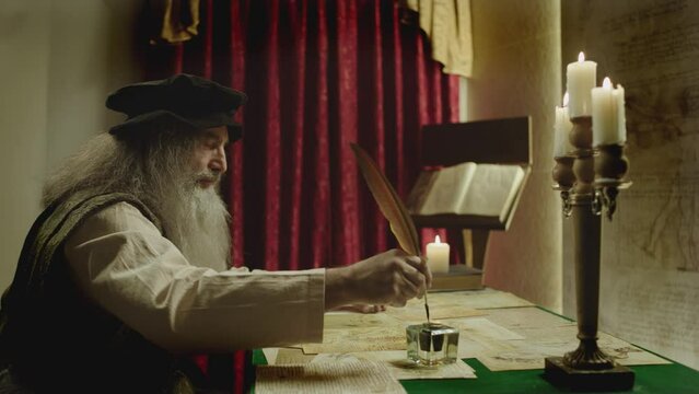 Old man with beard dressed like Leonardo Da Vinci writing , painting and working in vintage 15 - 16 century designed room . Big drawing of famous artwork  . Dipping ink pen on inkwell . Slow motion 