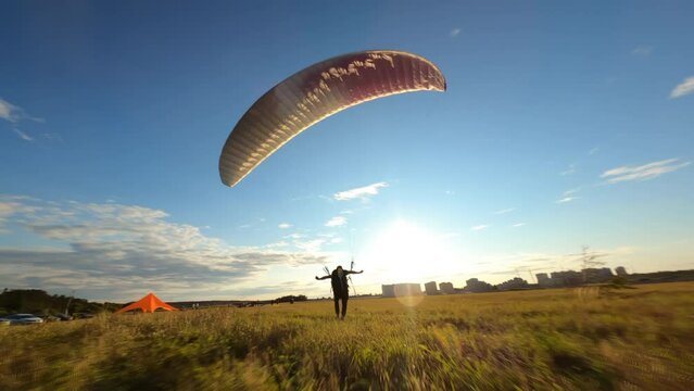 Paraglider lands on the green field against colourful sunset or sunrise