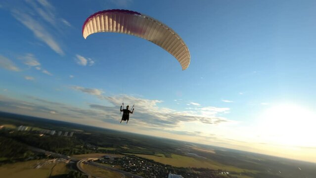 Dynamic aerial shot of paraglider flying along the river and against sunset sky 