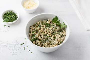 Pearl barley with cheese and herbs in white ceramic bowl on a light gray background, top view. Delicious and healthy breakfast