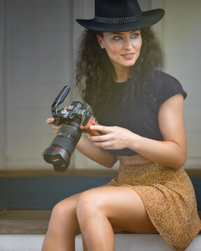 Portrait of a young elegant lady with a photo camera in a short skirt and t-shirt. Beautiful  female photographer  sits on the timber doorway. Portrait Photography. Port Douglas, QLD,Australia.