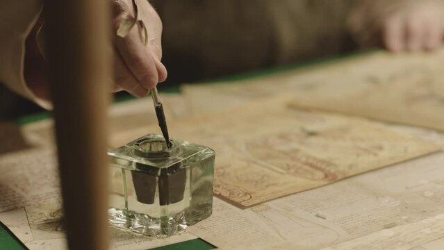 Old man with beard dressed like Leonardo Da Vinci writing , painting and working in vintage 15 - 16 century designed room . Big drawing of famous artwork  . Dipping ink pen on inkwell . Slow motion 