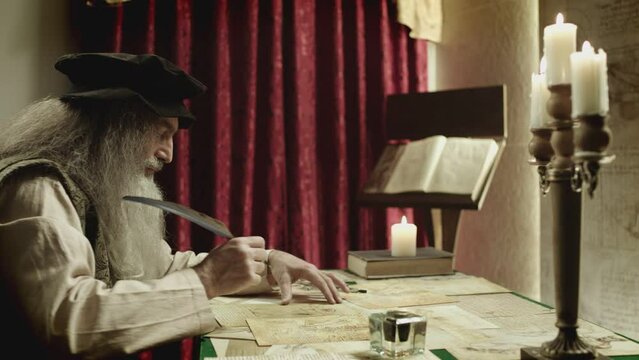 Old man with beard dressed like Leonardo Da Vinci writing , painting and working in vintage 15 - 16 century designed room . Big drawing of famous artwork  . Dipping ink pen on inkwell . Slow motion 