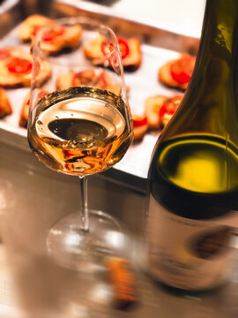 Ta&ccedil;a de vinho branco chardonnay com garrafa e bruschetta no p&atilde;o italiano ao fundo.