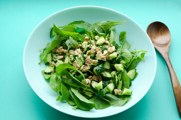 Vegetable salad with fresh arugula, cucumber in a plate with wooden spoon on turquoise background close-up. Vegetarian vitamin food salad. The concept of a healthy diet