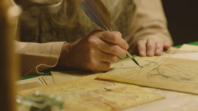 Old man with beard dressed like Leonardo Da Vinci writing , painting and working in vintage 15 - 16 century designed room . Big drawing of famous artwork  . Dipping ink pen on inkwell . Slow motion 