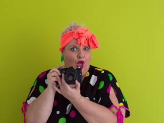 Obraz premium plus size smiling woman with funny emotional face expression with vintage camera in dress isolated on green background, traveler on vacation, summer fashion style, excited tourist.