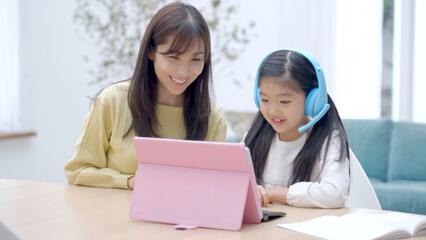 タブレットで通信教育を受ける女の子と見守るお母さん