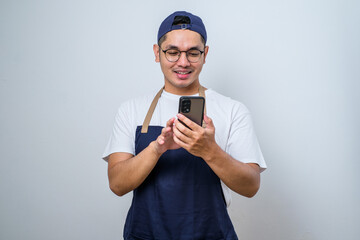 Young man barista man wearing apron work in coffee shop using mobile cell phone chat and smiling