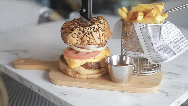 toma de video mostrando una deliciosa hamburguesa con papas fritas en plato de madera en restaurante.