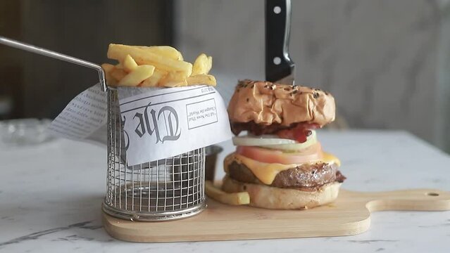 toma de video mostrando una deliciosa hamburguesa con papas fritas en plato de madera en restaurante.