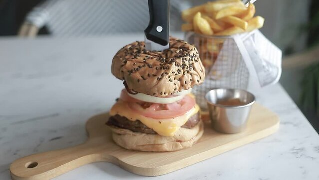 toma alejandose mostrando una deliciosa hamburguesa con papas fritas en plato de madera en restaurante.