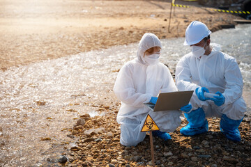 Biologist wear protective suit and mask collects sample of waste water from industry, problem environment, Ecologist sample taken dead fish to inspection and save data to laptop computer, Toxic water