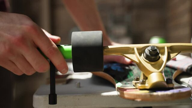 Man's hands as he uses tool to unscrew longboard wheel.