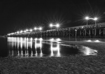 The lights of Pier at night reflected in the wet sand on the beach. Wooden pier at White Rock BC, Canada