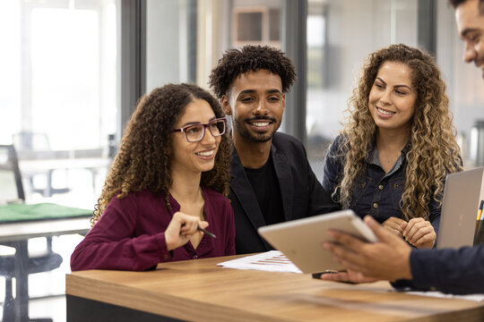 Quatro Jovens Sentados Ao Redor De Uma Mesa Falando Sobre Negócios