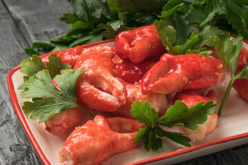 Crab claws in oil with parsley leaves on a wooden table.