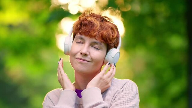 Non-binary gender person listening to music with closed eyes in a park