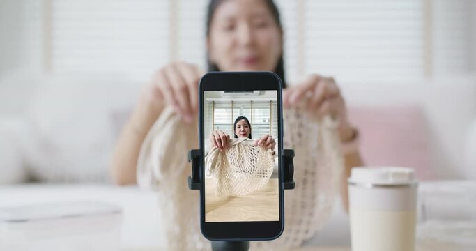 Asia girl vlogger youtuber influencer review eco friendly reuse product glass box, bottle, mesh bag on reel tiktok instagram app sit record vlog blog selfie live talk show look at camera at home sofa.