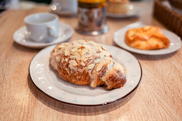 A fresh large croissant on a beautiful plate in a cafe or restaurant. Close-up of a croissant and cream sprinkled with nuts. Sweet and delicious dessert for coffee time.