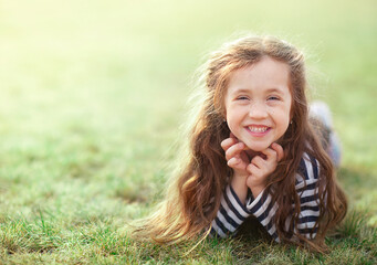 Naklejka premium a little girl with long fluffy hair is now lying on the grass and laughing looking at the camera
