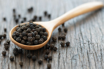 Whole black peppercorn in a wooden spoon on wooden background.