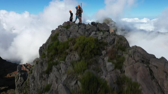 Drone shot moving up and forward, revealing 3 friends on the peak of Pico das Torres in Madeira.
