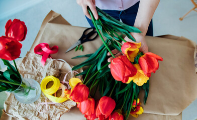 Women's hands pack a festive bouquet in wrapping paper. The florist makes an assembly with red...