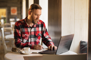 businessman working with documents and laptop in cafe. bearded blogger in plaid shirt taking notes in cafeteria