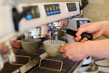 Close-up of professional barista holding cup and preparing coffee in a carob coffee machine in cafe - obrazy, fototapety, plakaty